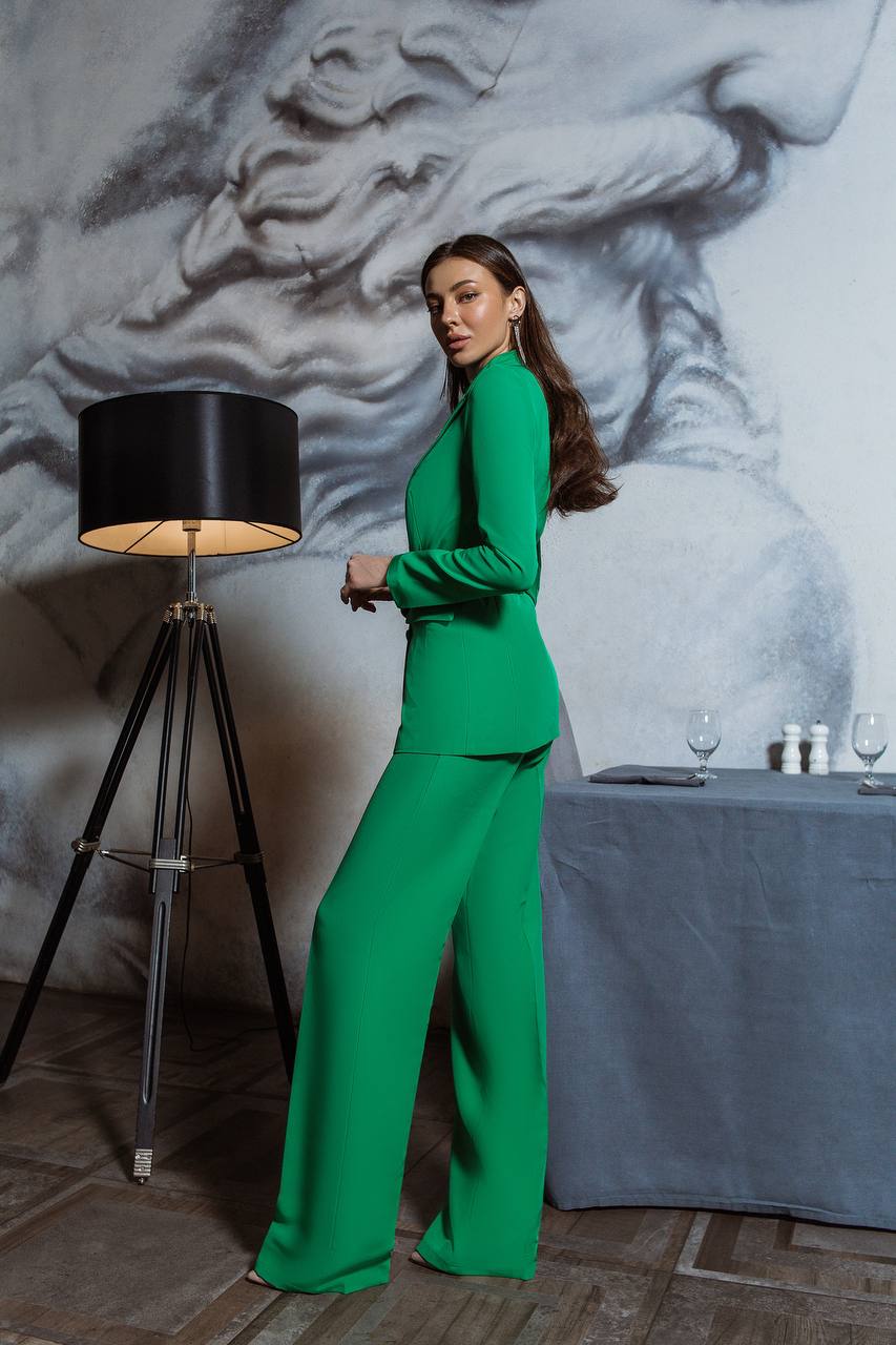 Woman in a green outfit standing in a room with a lamp and table.