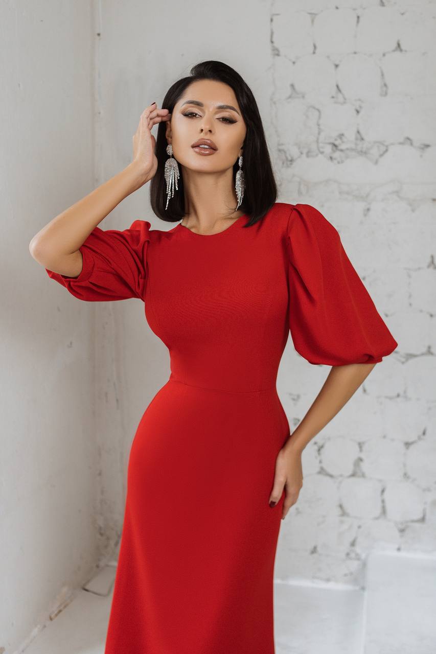 Woman wearing a red dress with puffed sleeves against a white brick wall.