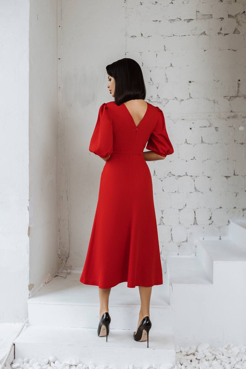 Woman in a red dress standing against a white textured wall.