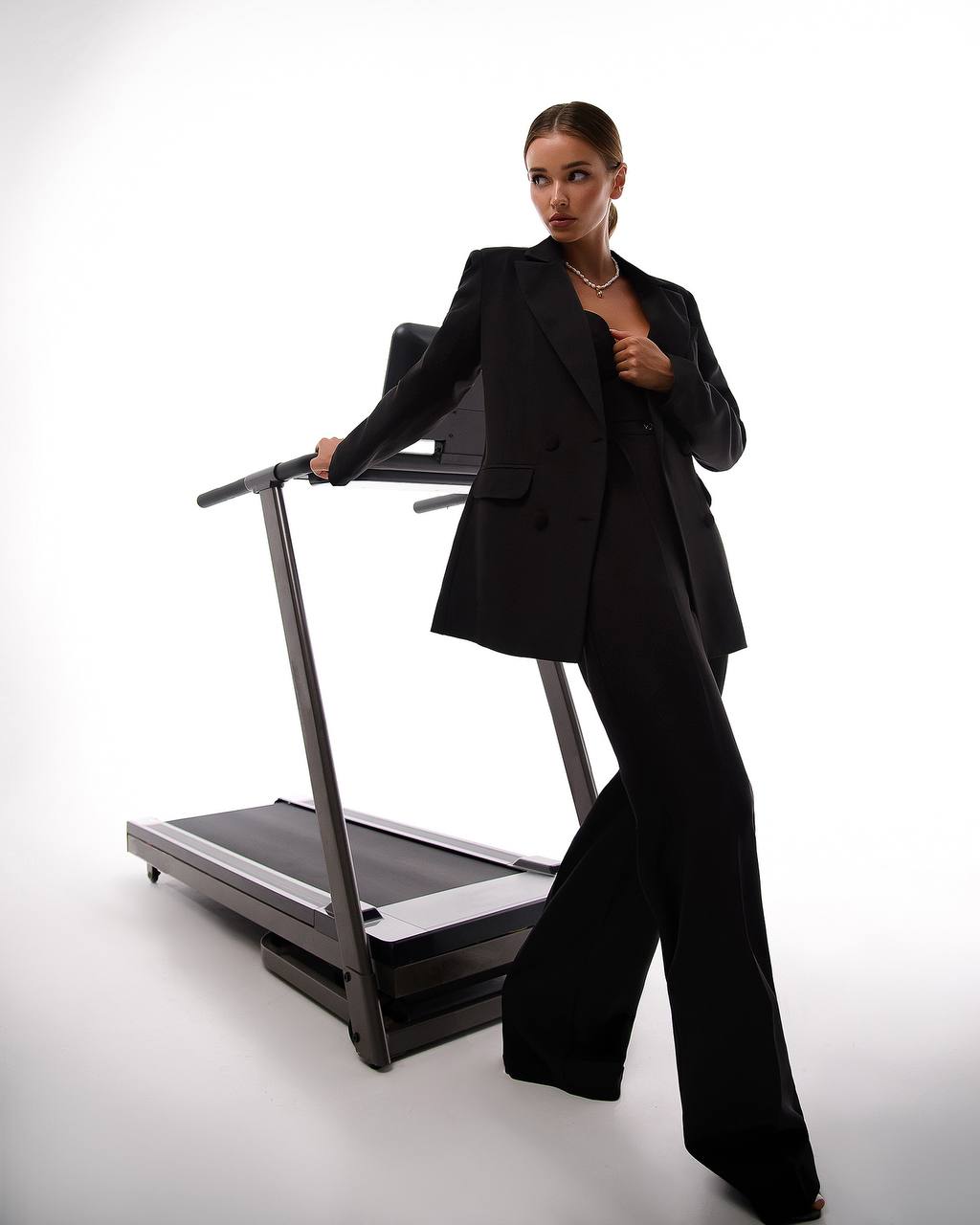 Person in a black suit standing next to a treadmill on a white background