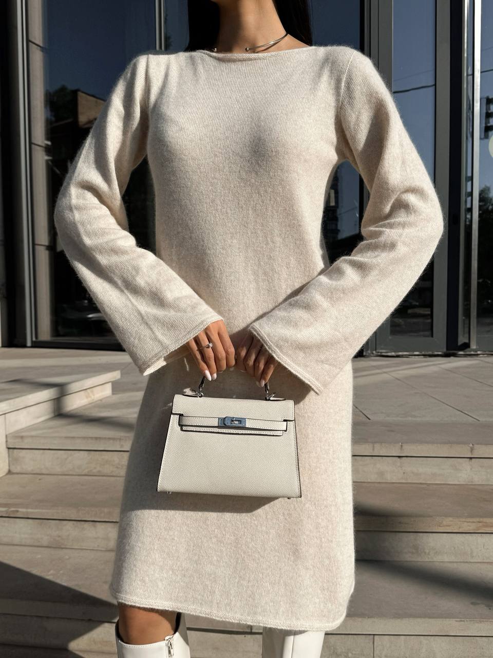 Person wearing a light gray dress holding a matching handbag on a wooden deck.