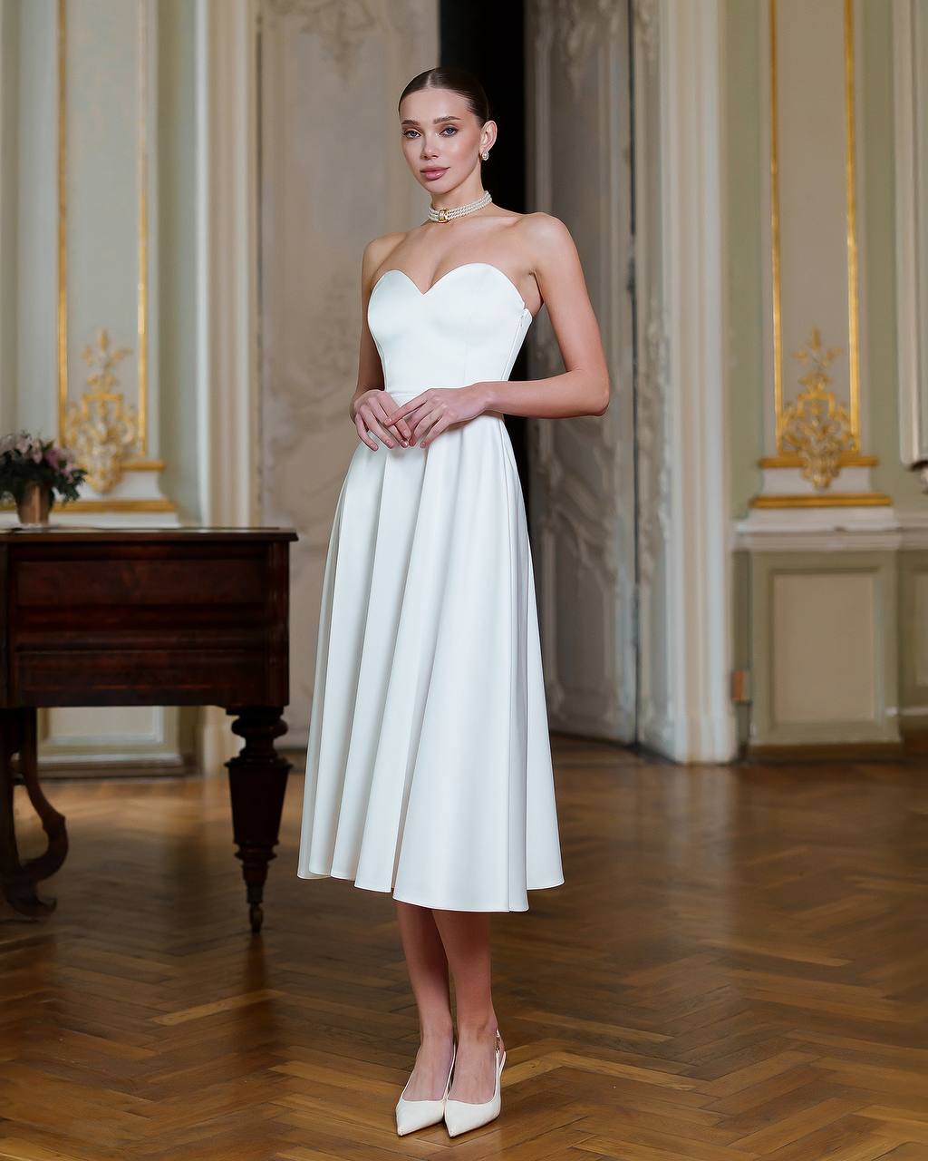 Woman in a white strapless dress standing in an elegant room with a piano.