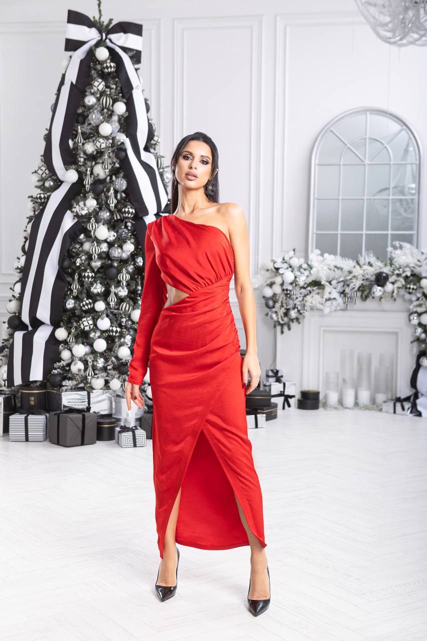 Woman in a red one-shoulder dress standing in a decorated room with Christmas tree and fireplace.