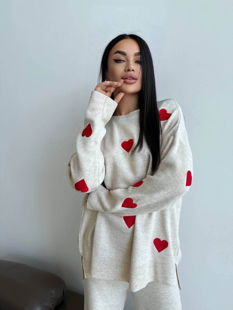 Woman wearing a white sweater with red heart patterns against a plain background