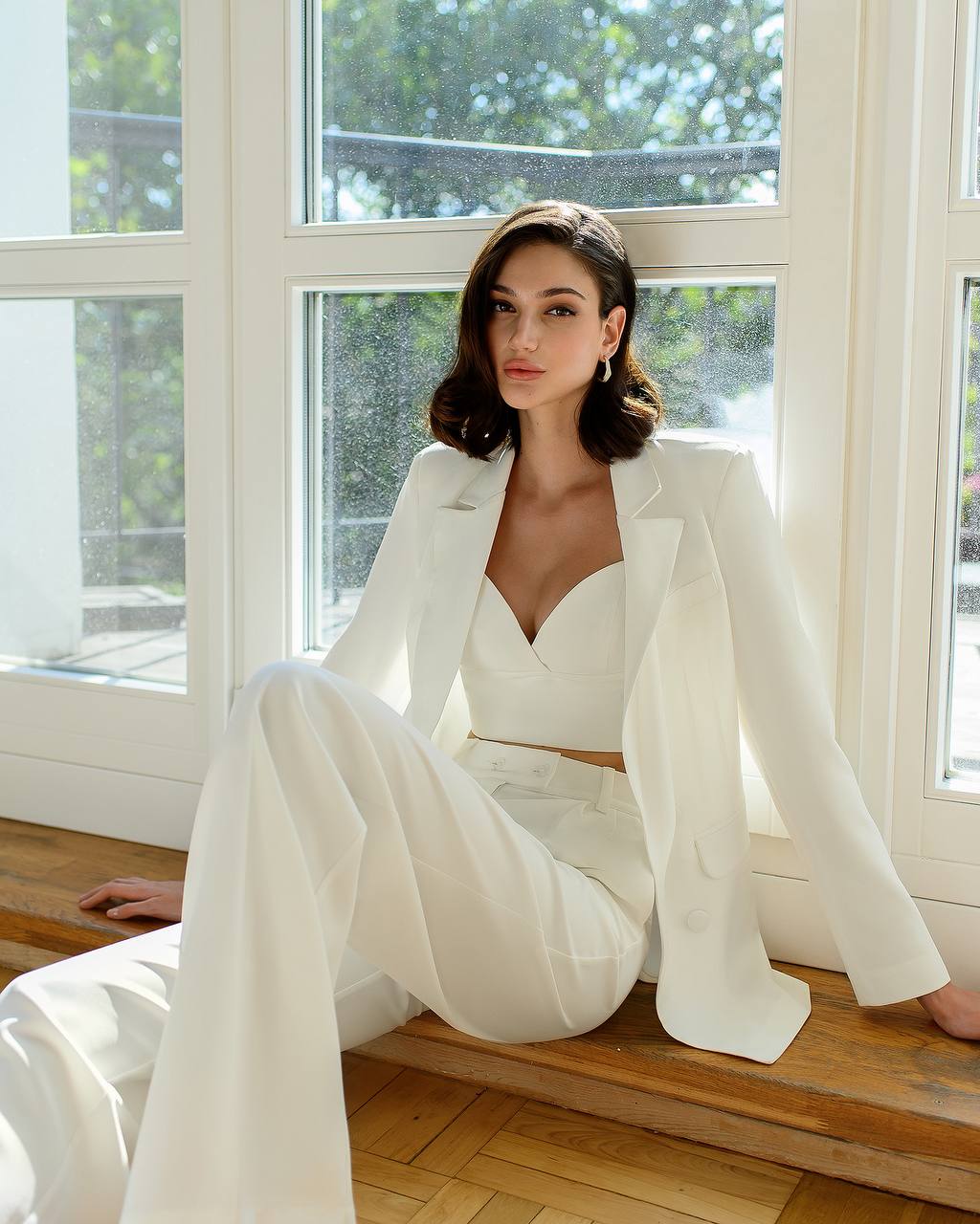 Woman in a white outfit sitting by a window with natural light