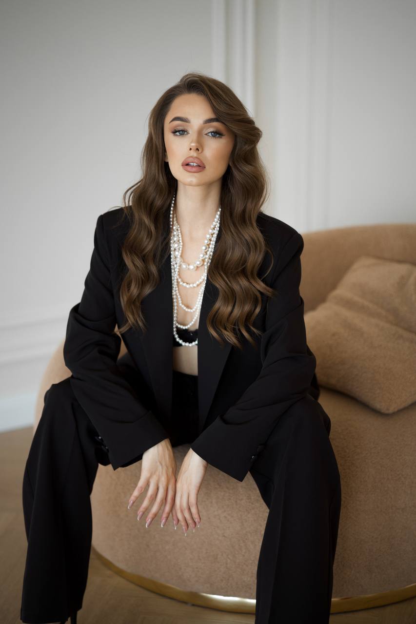 Woman in a black suit sitting on a beige couch with a neutral background