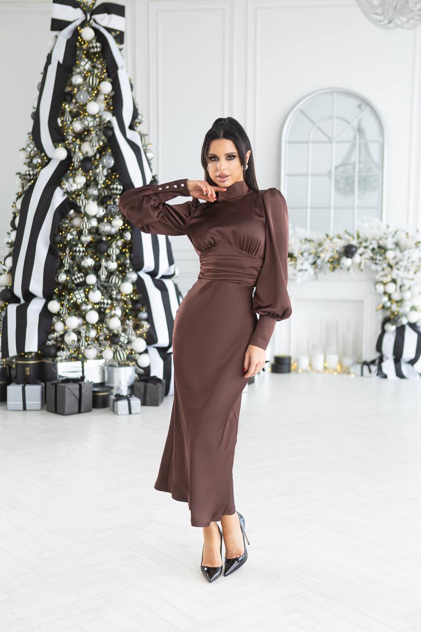 Woman in a brown dress standing in a decorated room with Christmas tree and gifts.