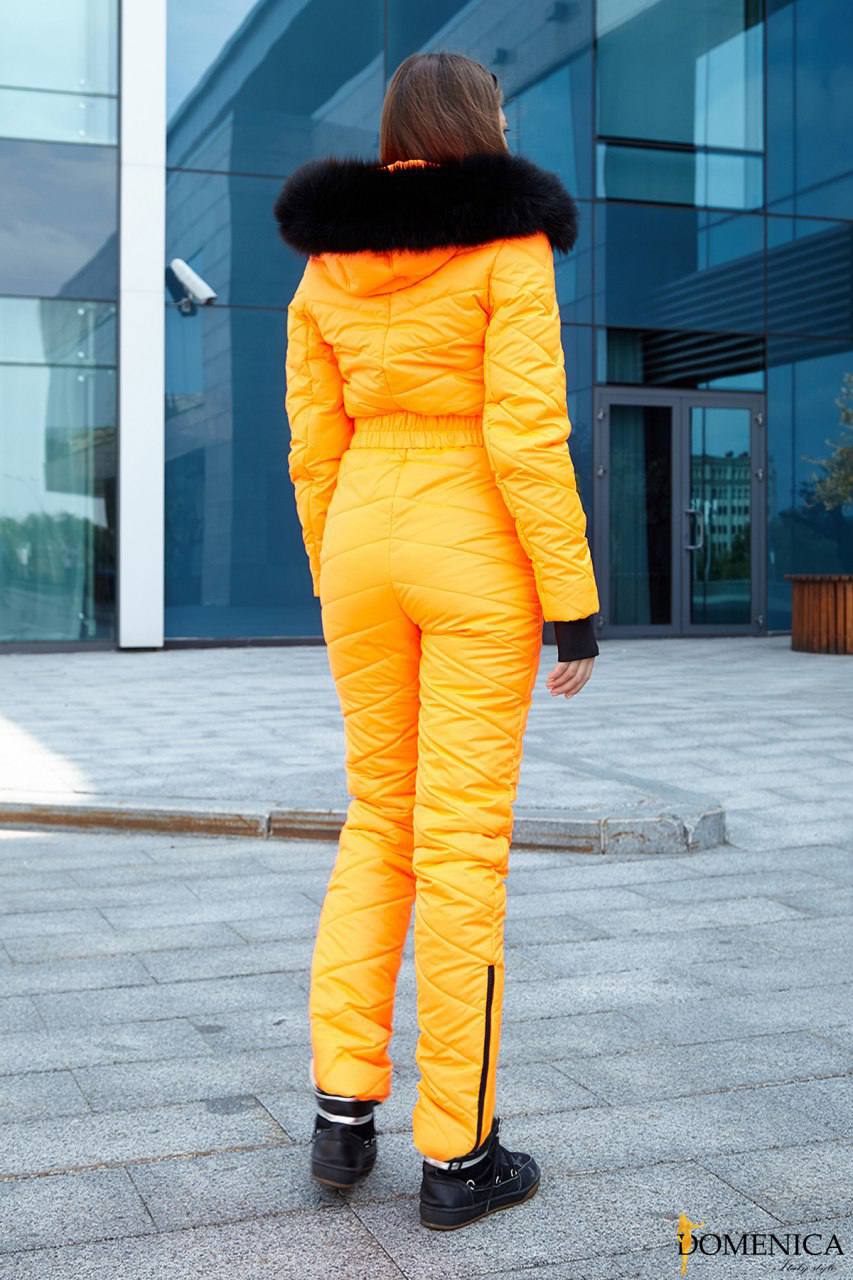 Person wearing a bright yellow puffer suit with black fur hood in front of a modern building.