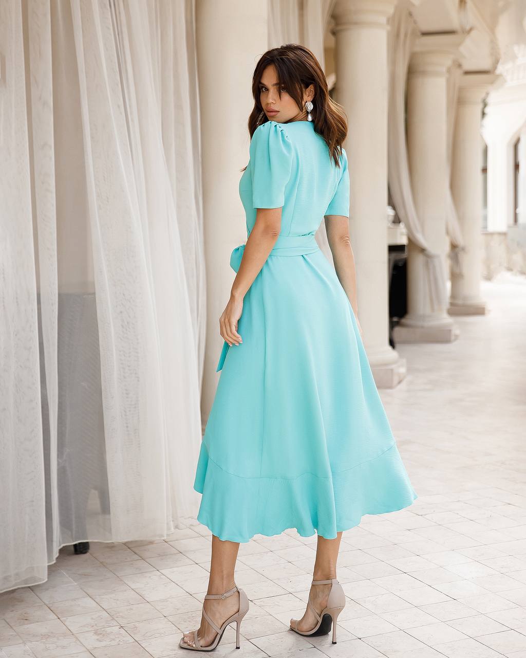 Woman in a light blue dress standing in an elegant indoor setting with columns.