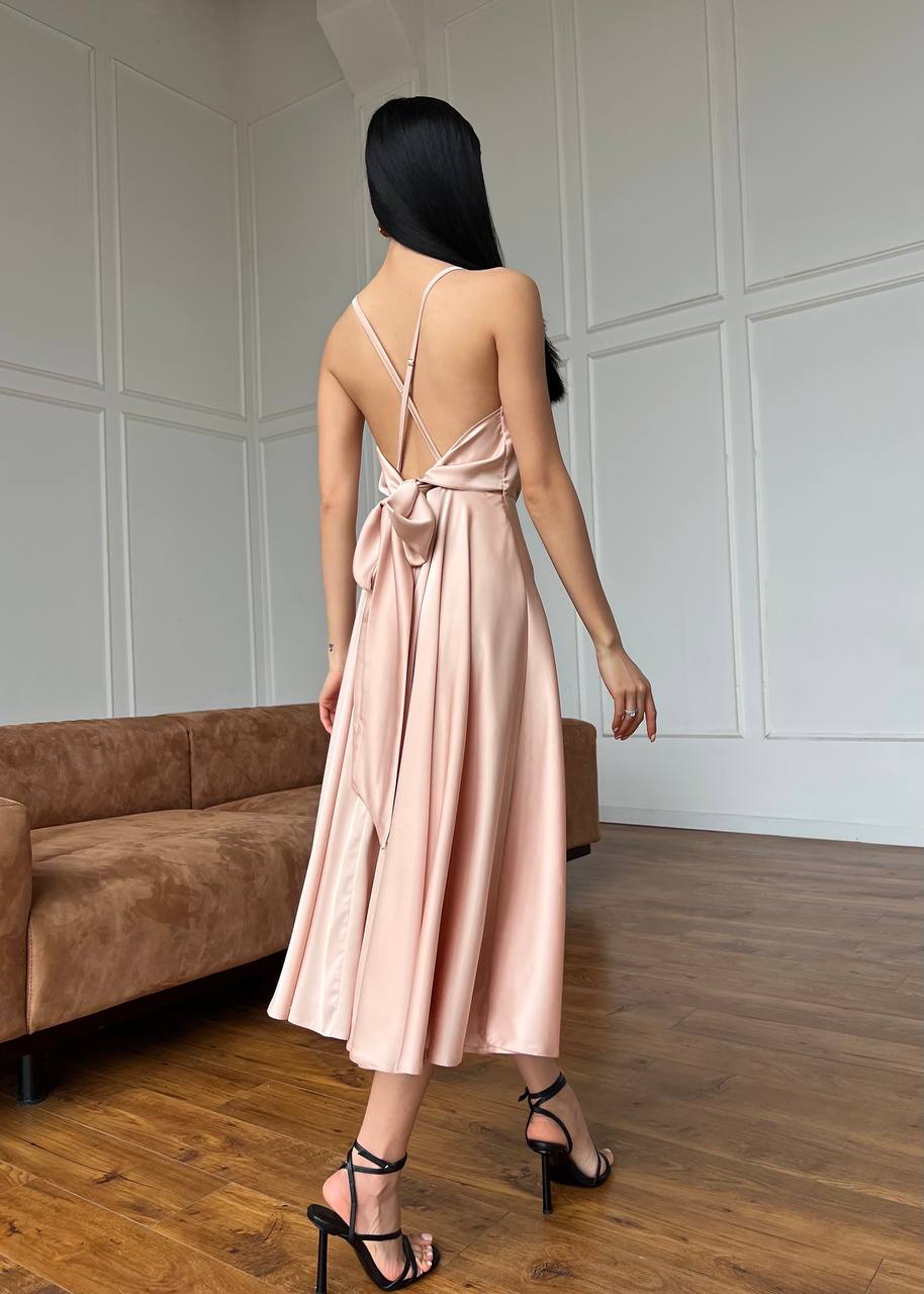 Woman in a pink dress standing in a room with wooden flooring and a brown sofa.