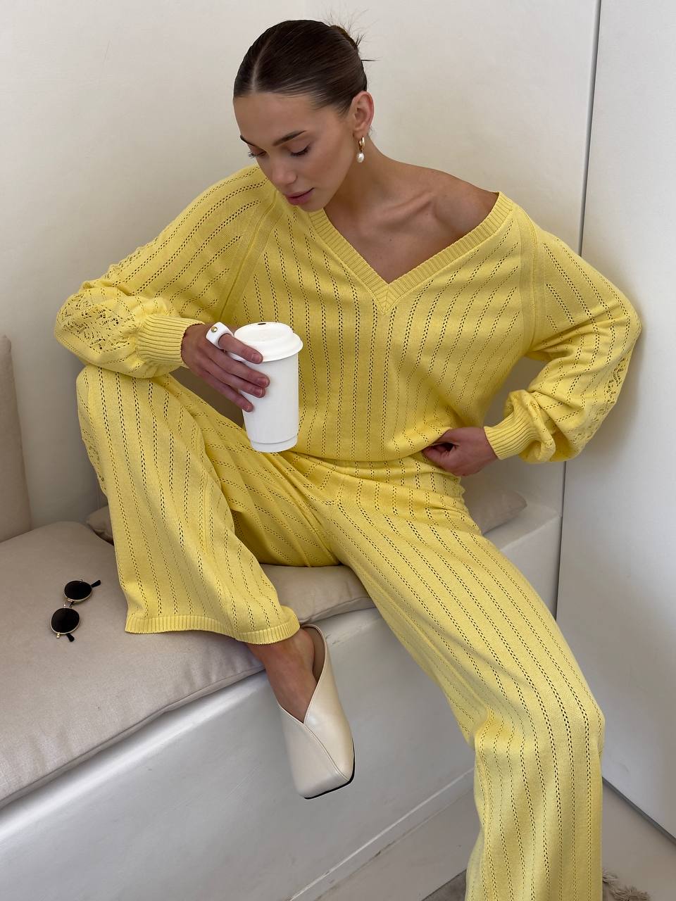 Woman in a yellow outfit sitting on a white surface holding a white cup.