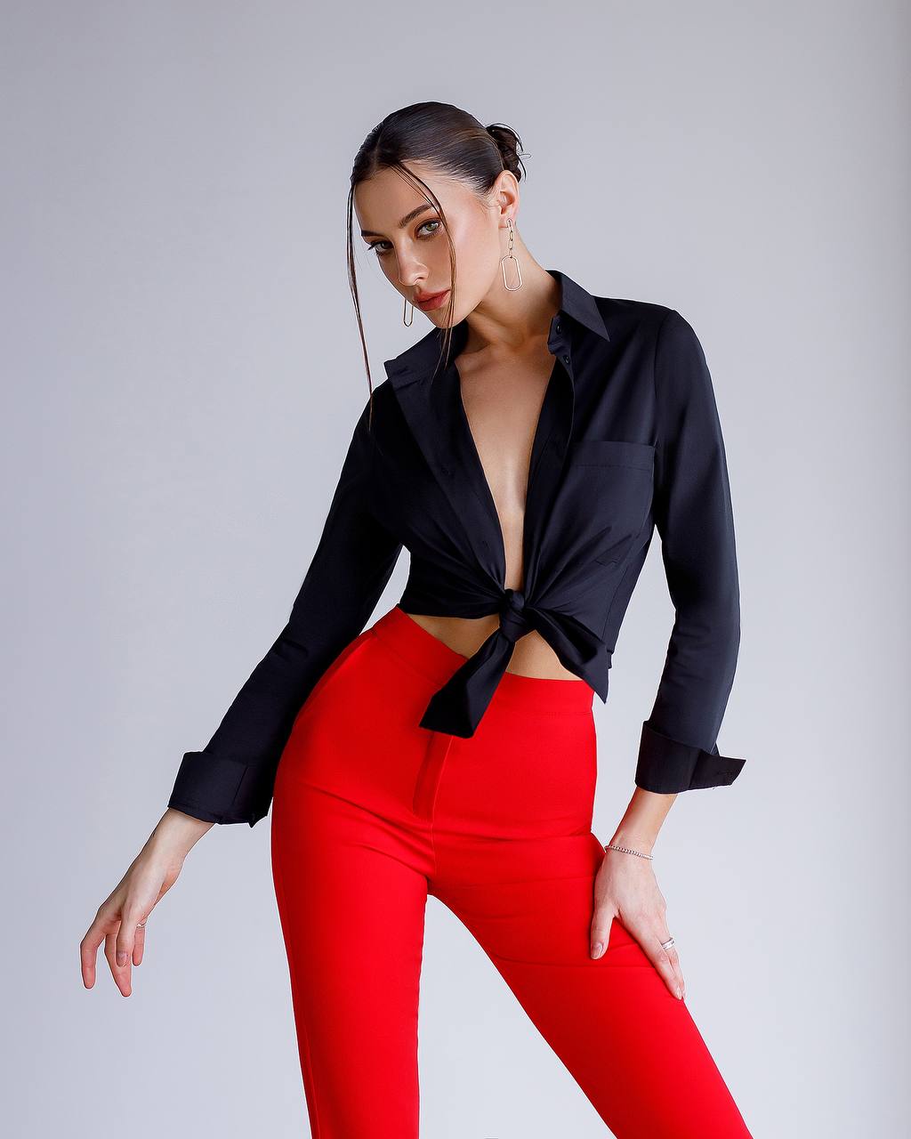 Woman wearing a black tied blouse and red pants on a gray background