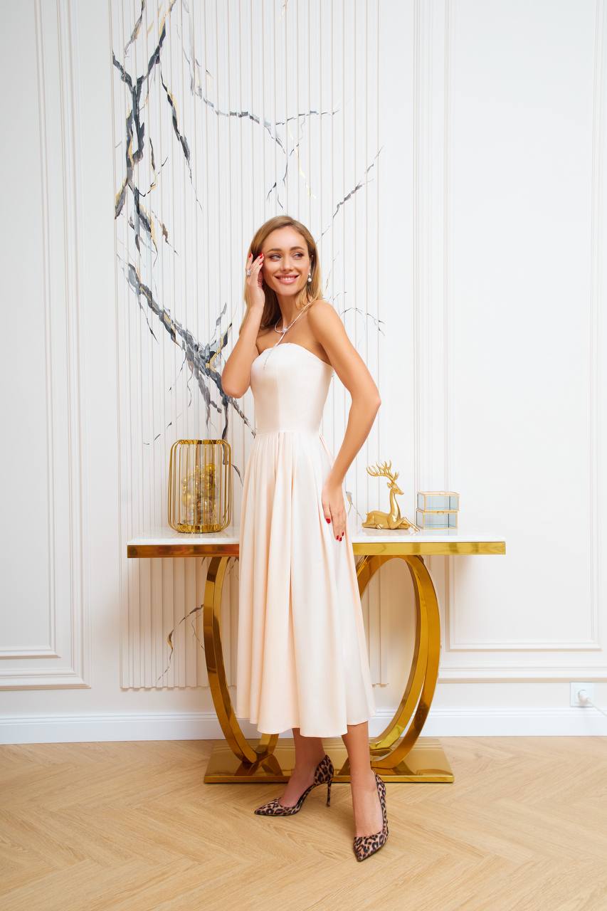 Woman in a white dress standing in a stylish interior setting with marble wall and gold table.
