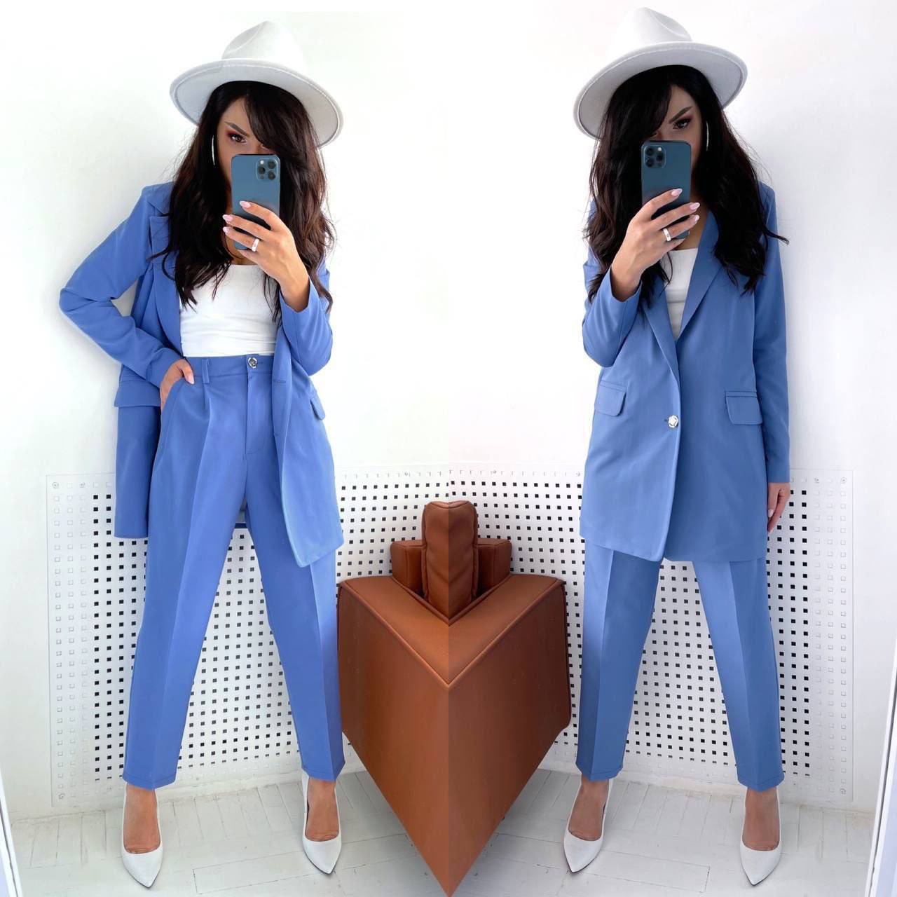 Woman in a blue suit and white hat taking a mirror selfie.