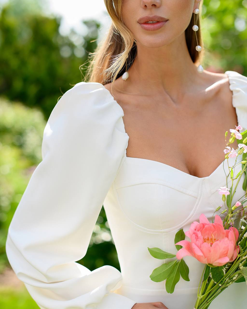 Woman in a white dress holding pink flowers with a blurred green background