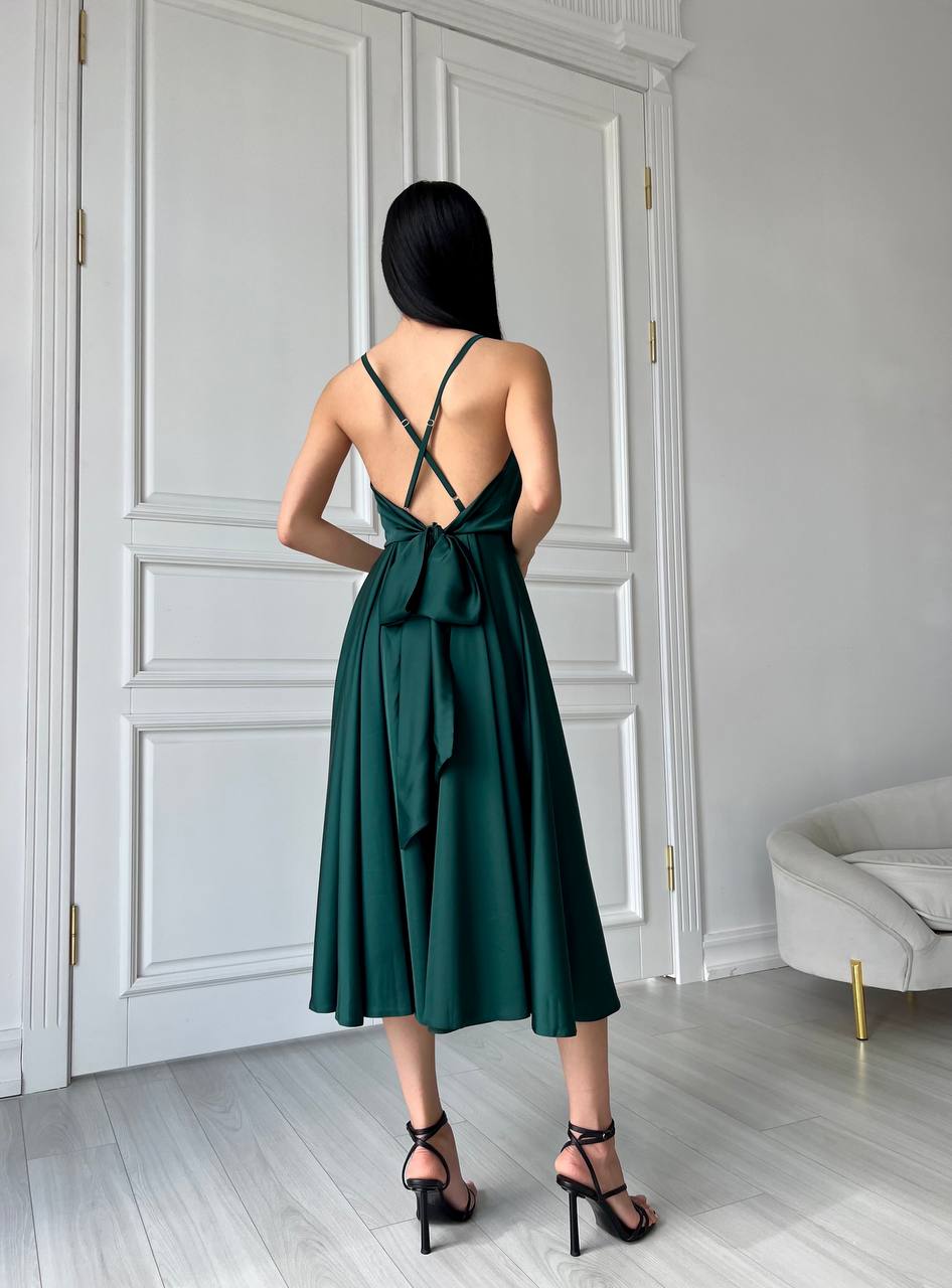 Woman wearing a green dress with a back bow in a room with white walls and a gray sofa.