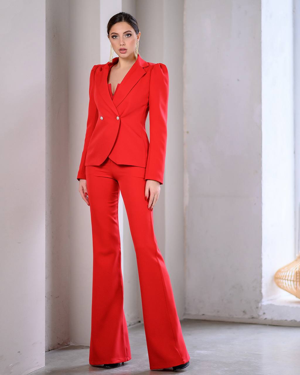 Woman wearing a red suit standing against a light-colored wall.