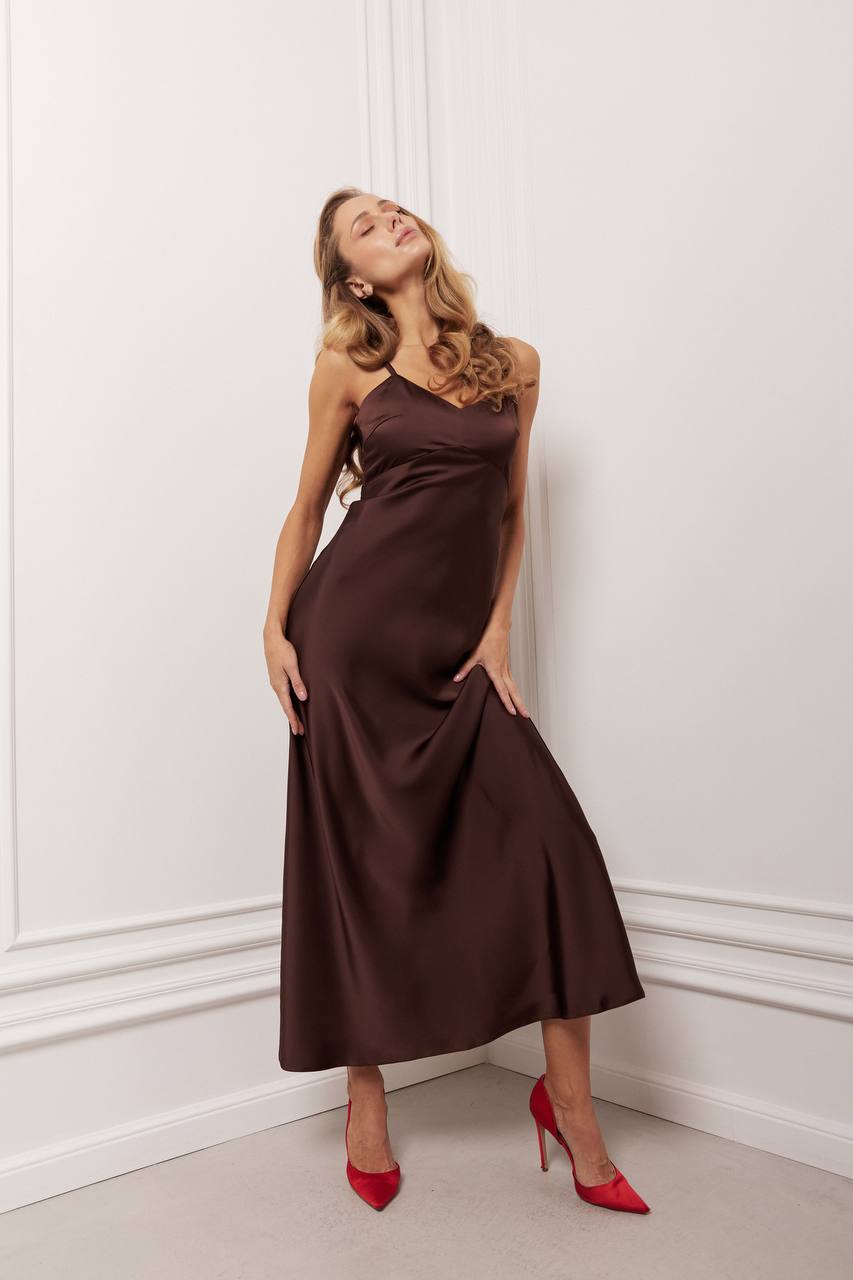 Woman wearing a brown dress with red shoes against a white wall