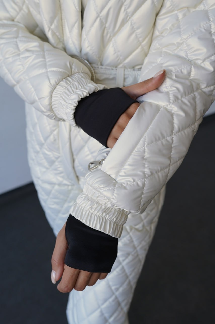 Person wearing a white quilted jacket and black gloves indoors.