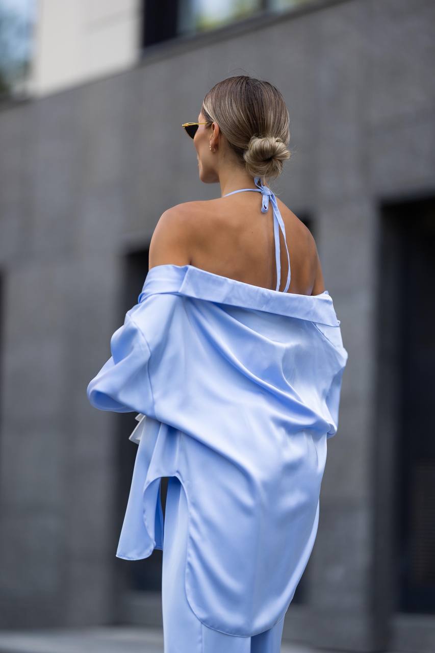Woman wearing a light blue off-shoulder outfit against a gray wall.