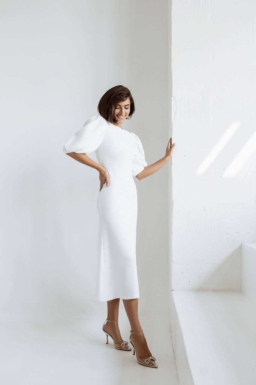 Woman wearing a white dress standing against a white wall