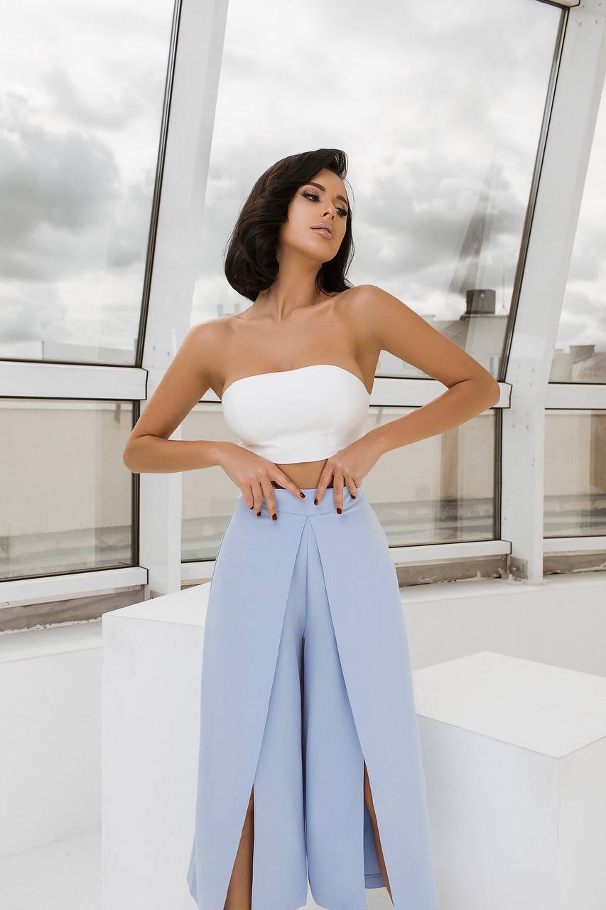 Woman wearing a white top and light blue pants standing on a rooftop with a cityscape background.