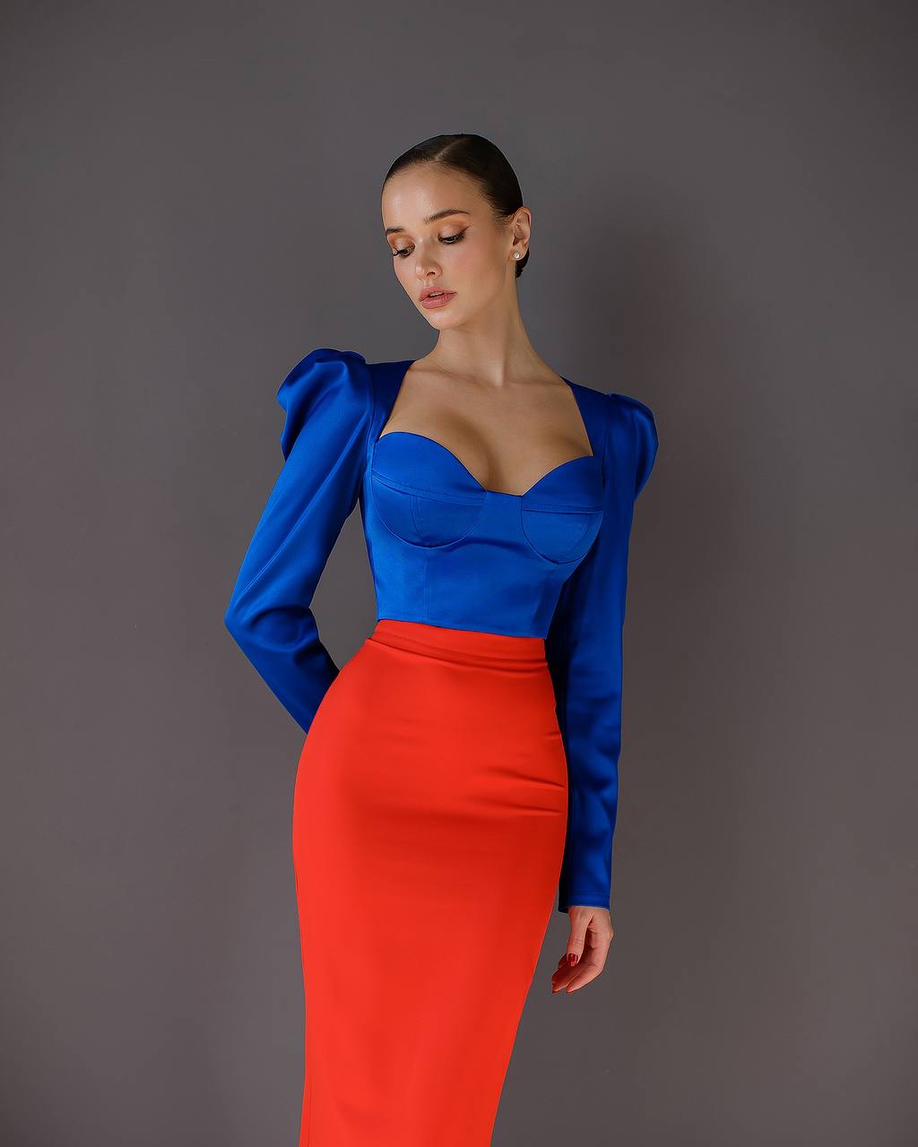 Woman wearing a blue top and red skirt against a gray background