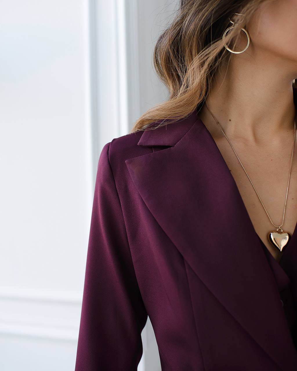 Close-up of a person wearing a purple blazer and gold necklace with a heart pendant.