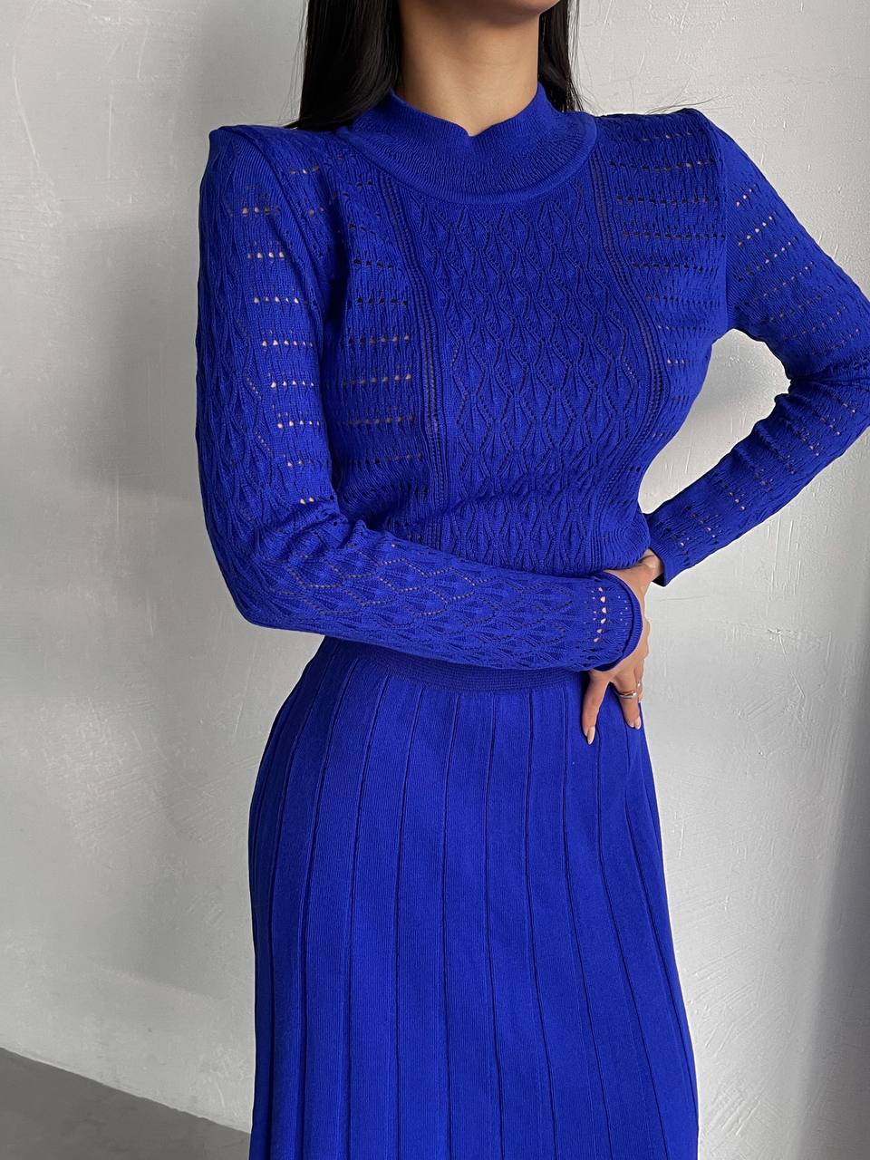 Person wearing a blue dress with long sleeves against a plain background