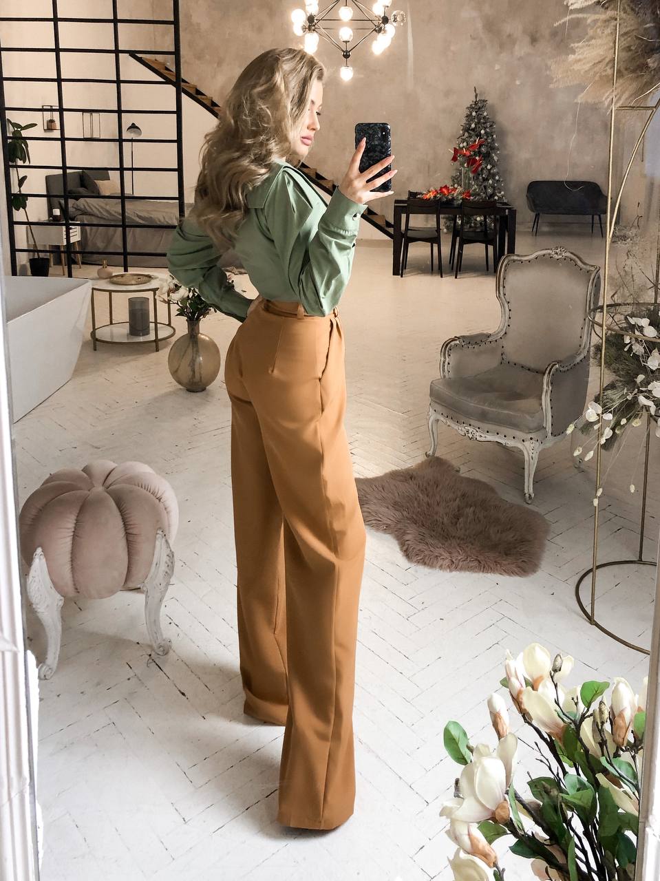 Woman taking a mirror selfie in a stylish room with decor elements.