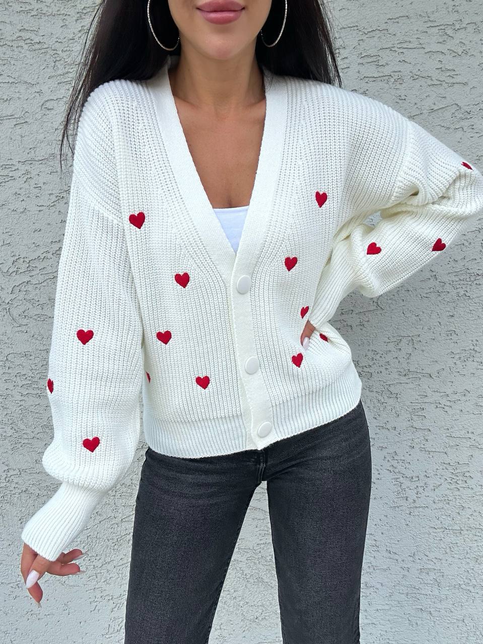 White cardigan with red heart patterns worn by a person against a gray background