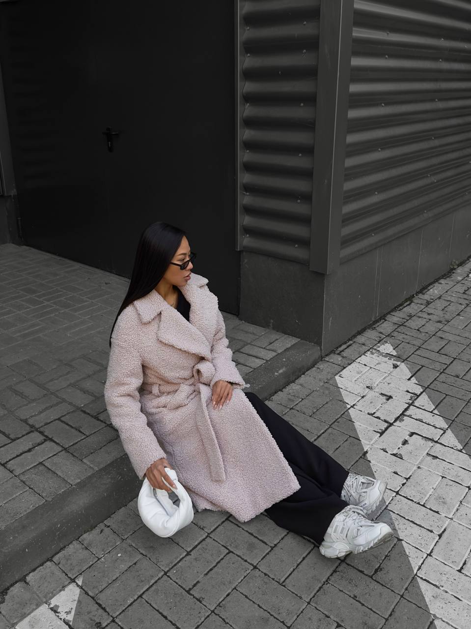 Woman in a pink coat sitting on a step outdoors.