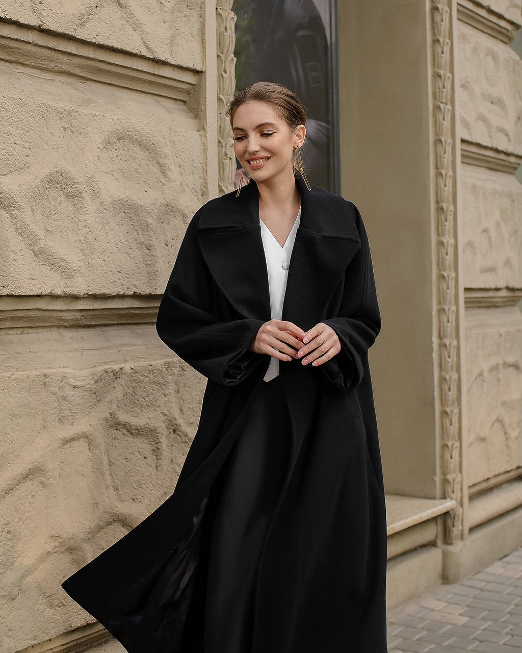 Woman wearing a black coat standing against a stone building.