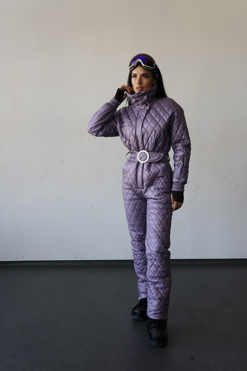 Person wearing a purple quilted snowsuit with goggles on a plain background