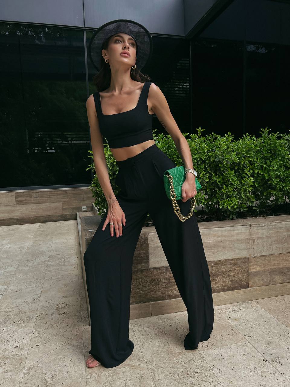 Woman in black outfit with wide-leg pants and a crop top, standing outdoors.