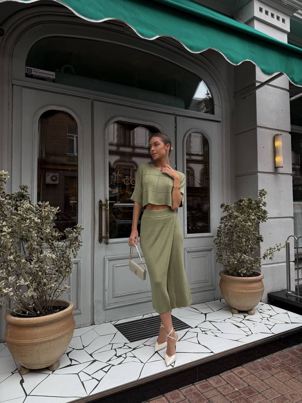 Woman in a green outfit standing in front of a store with a green awning.