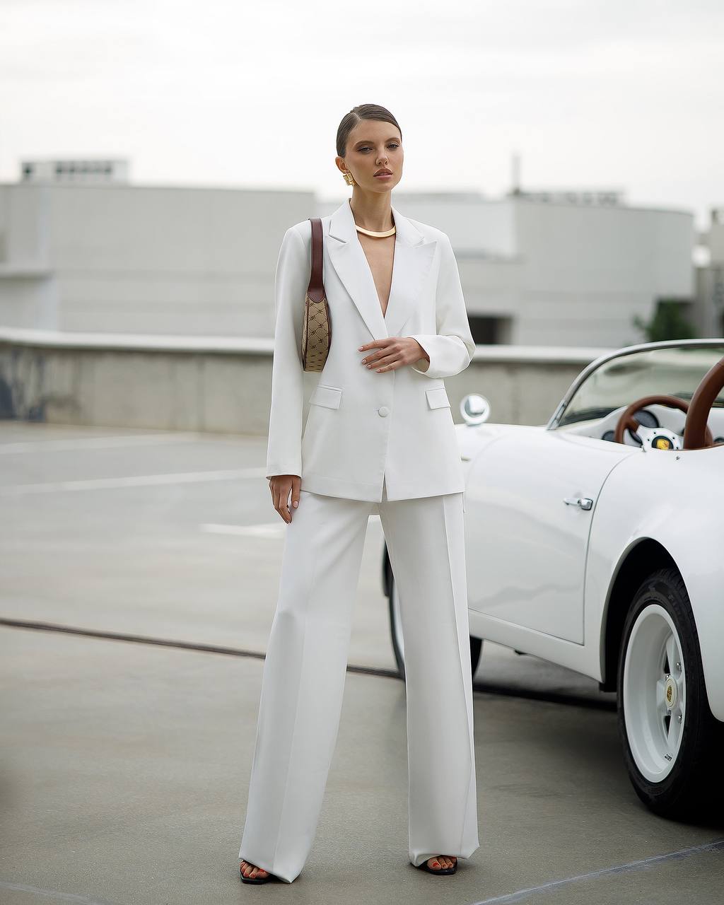 Woman in a white suit standing next to a white car with a blurred background