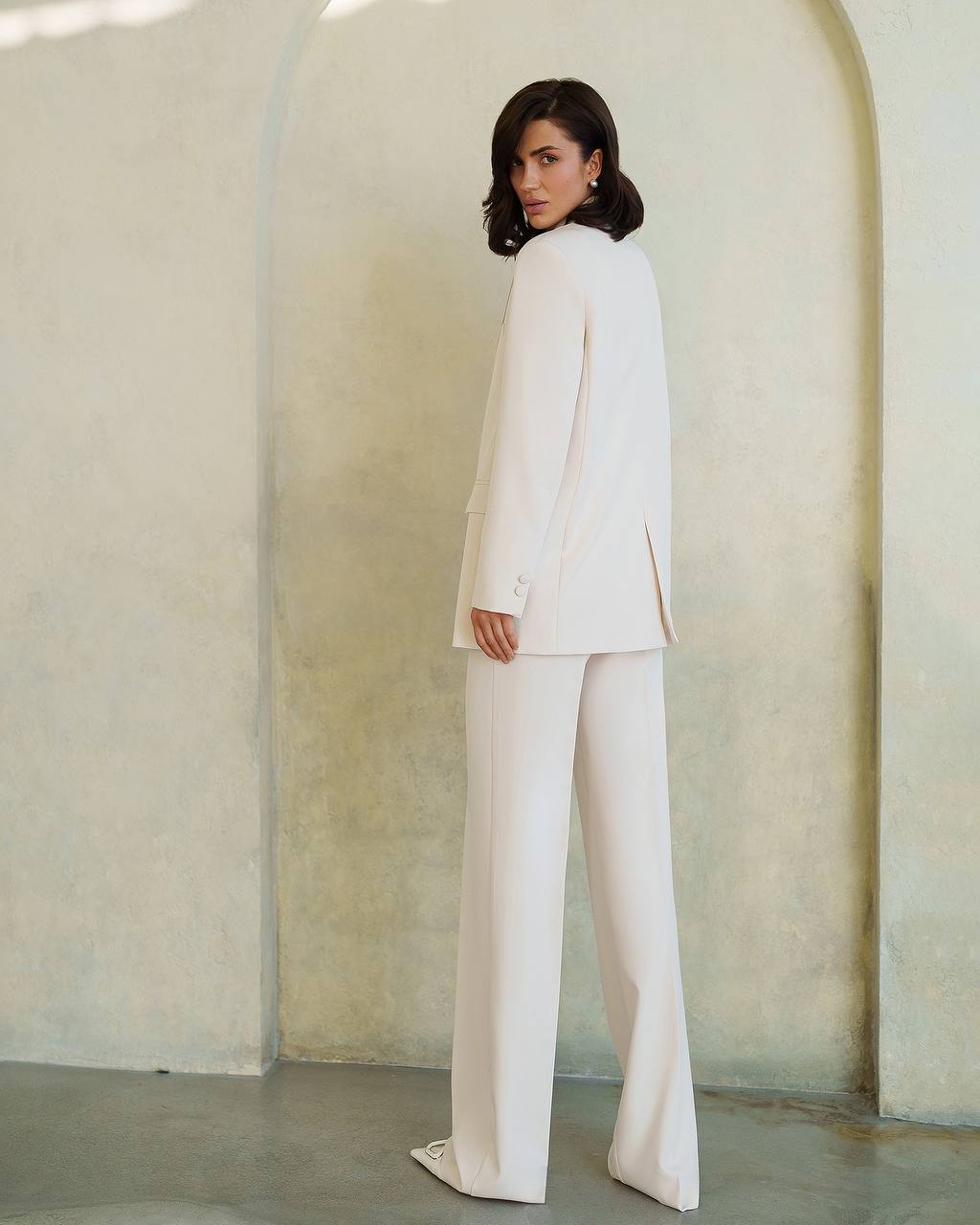 Woman wearing a white suit standing against a neutral background