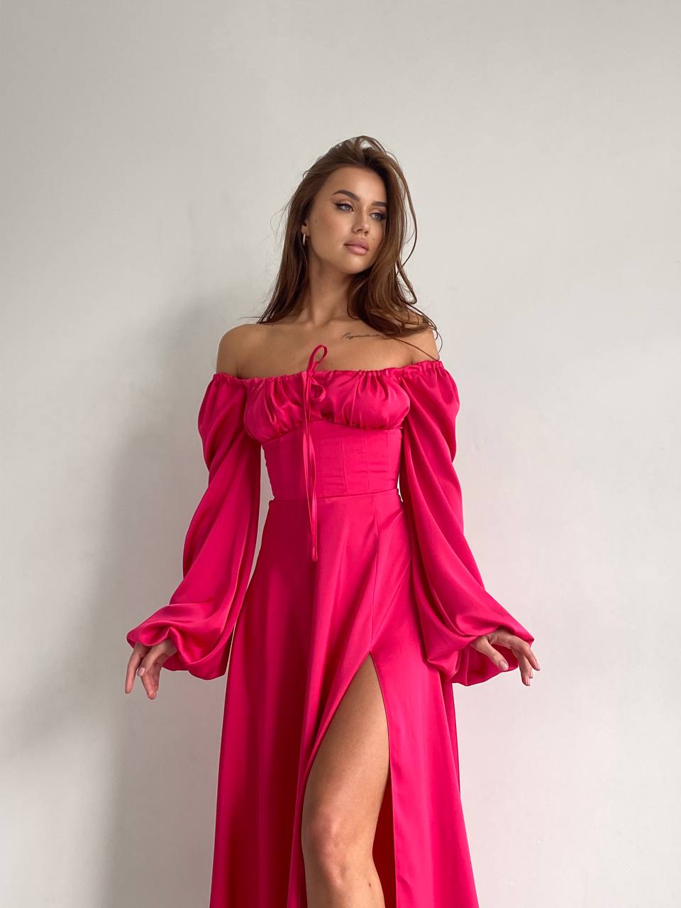 Woman wearing a bright pink off-shoulder dress with long sleeves on a plain background