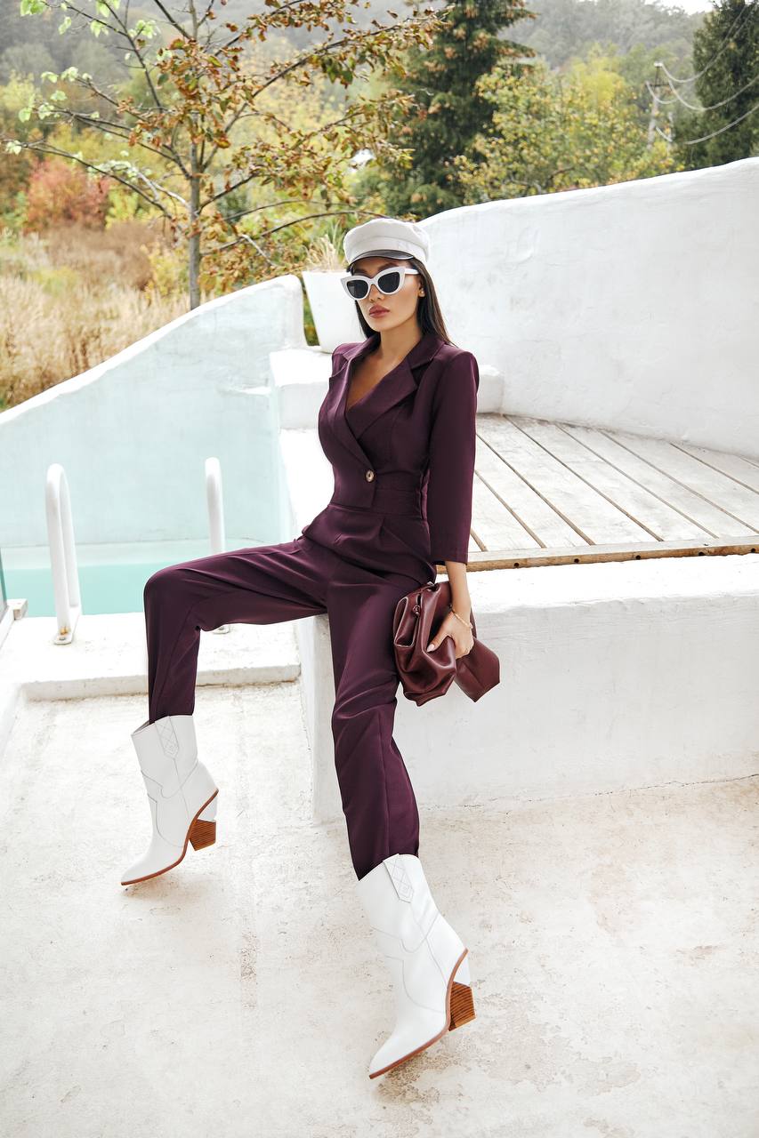 Woman in a purple outfit with white boots sitting on a white bench outdoors.