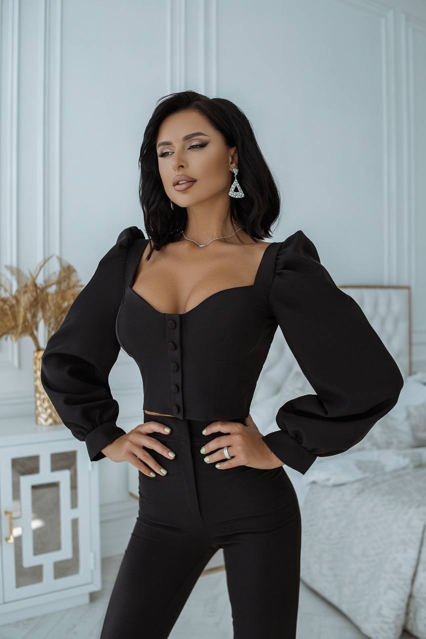 Woman wearing a black outfit with puffed sleeves in an elegant room.