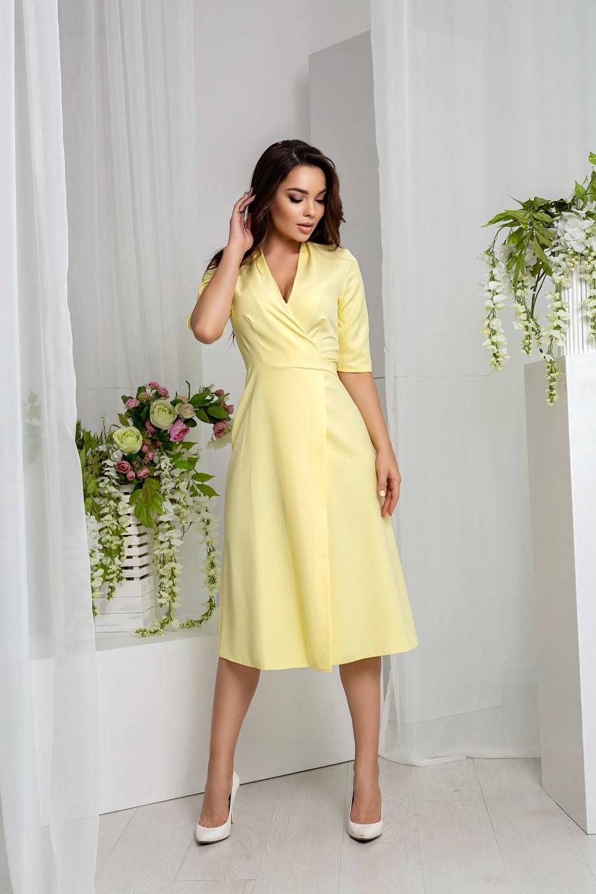 Woman in a yellow dress standing in a bright room with white curtains and floral decorations.