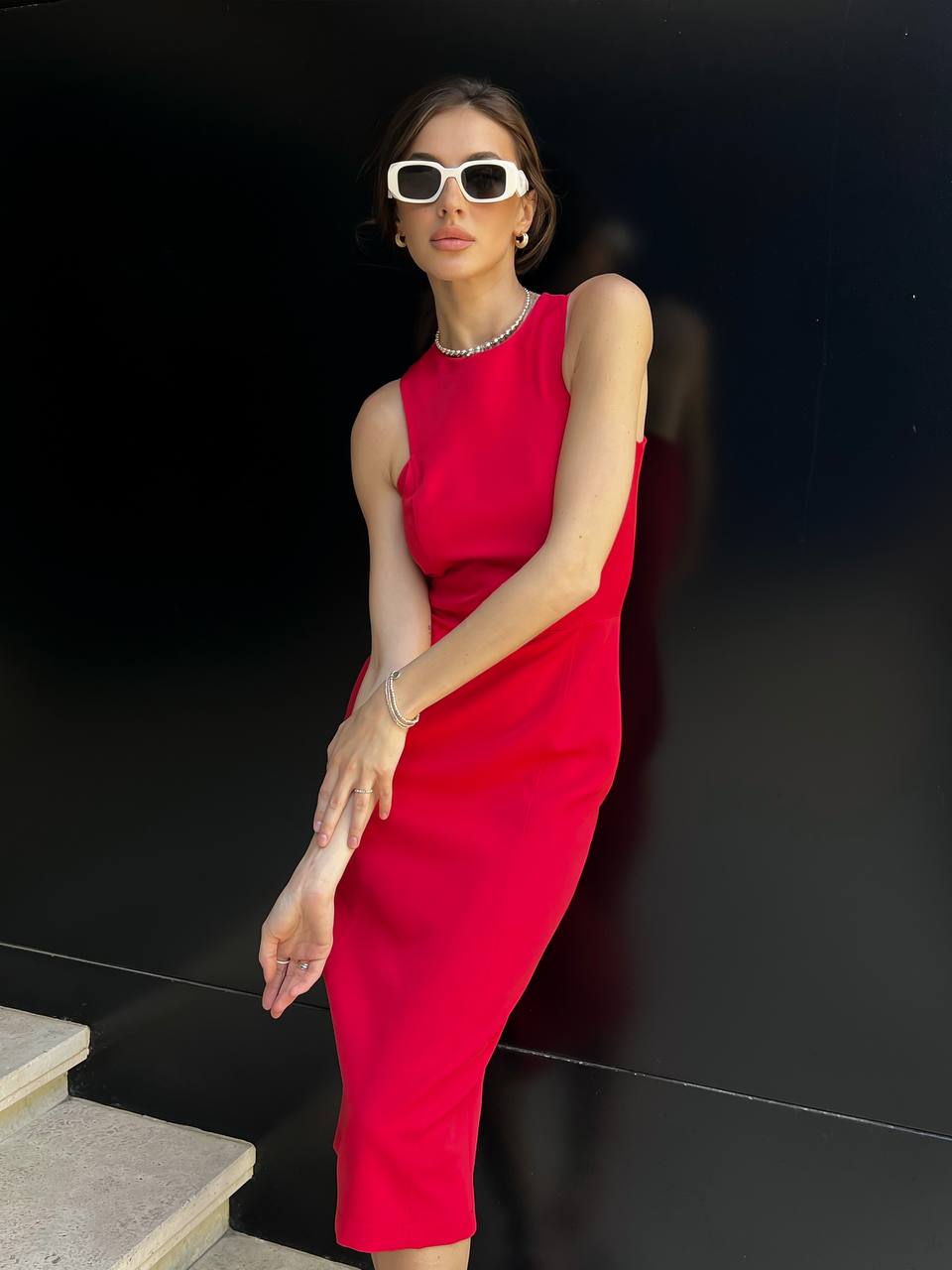 Woman in a red dress and sunglasses posing against a black background