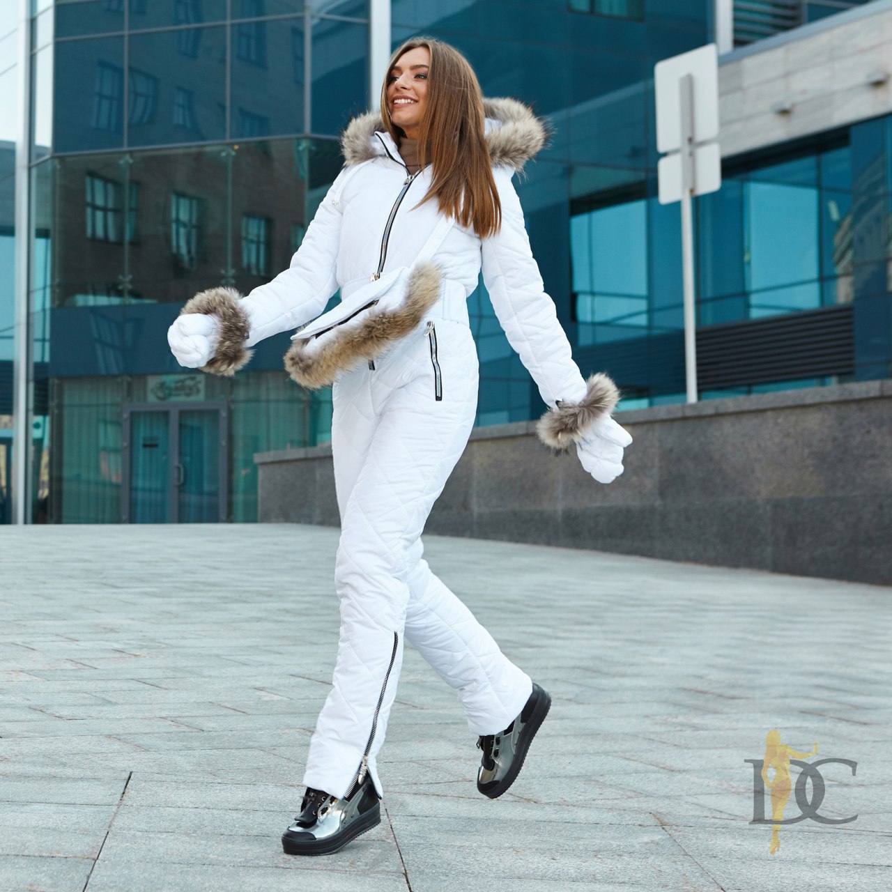 Woman in a white winter outfit with fur accents walking outdoors.