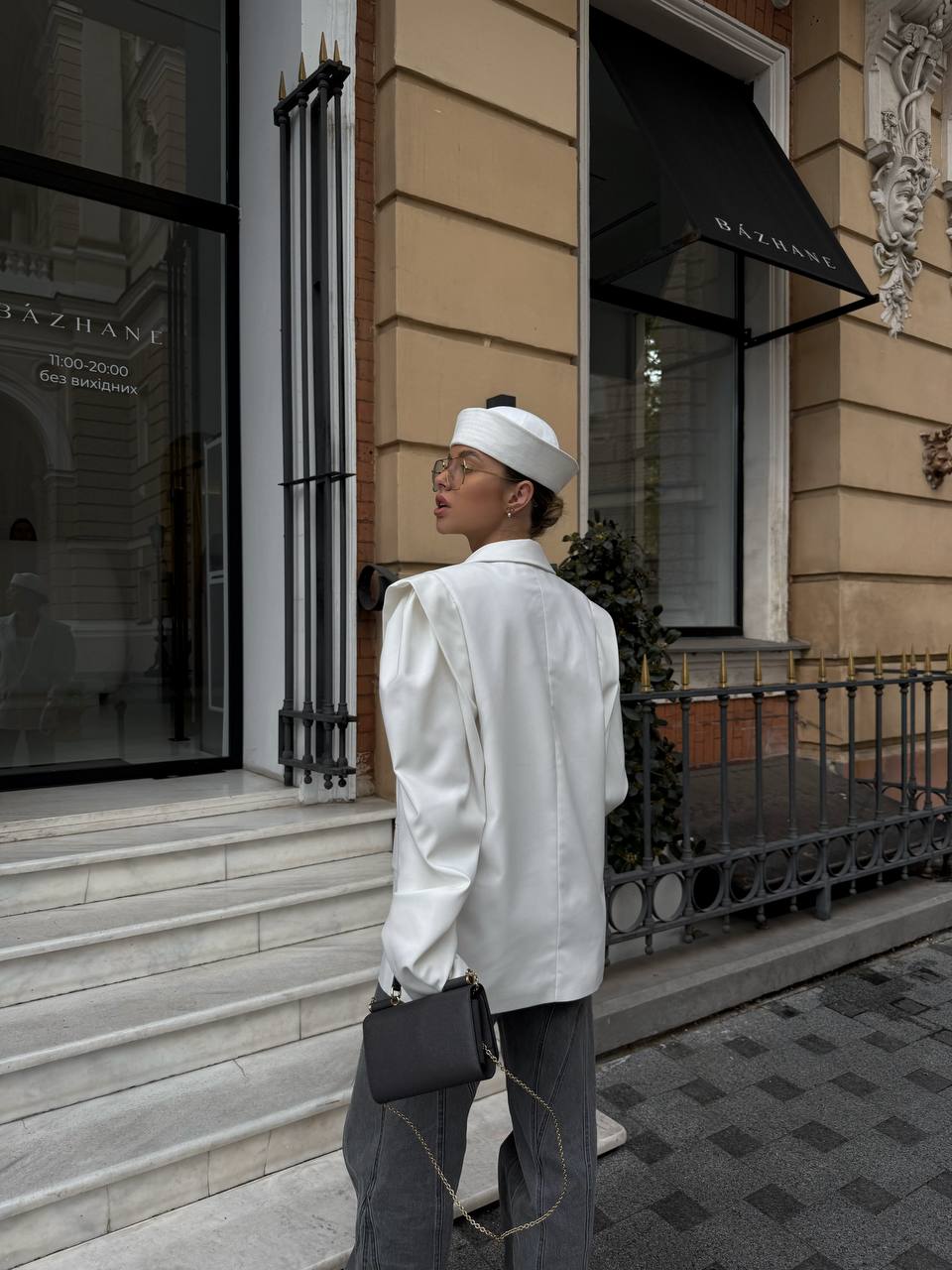 Person in a white outfit standing on a city street with a building in the background