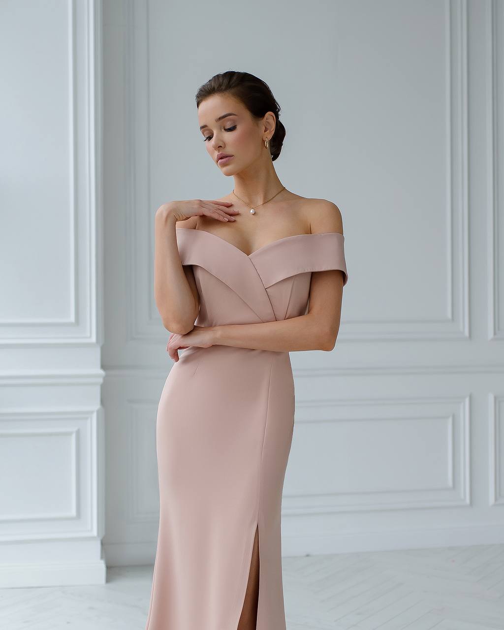 Woman wearing a pink off-shoulder gown against a white wall