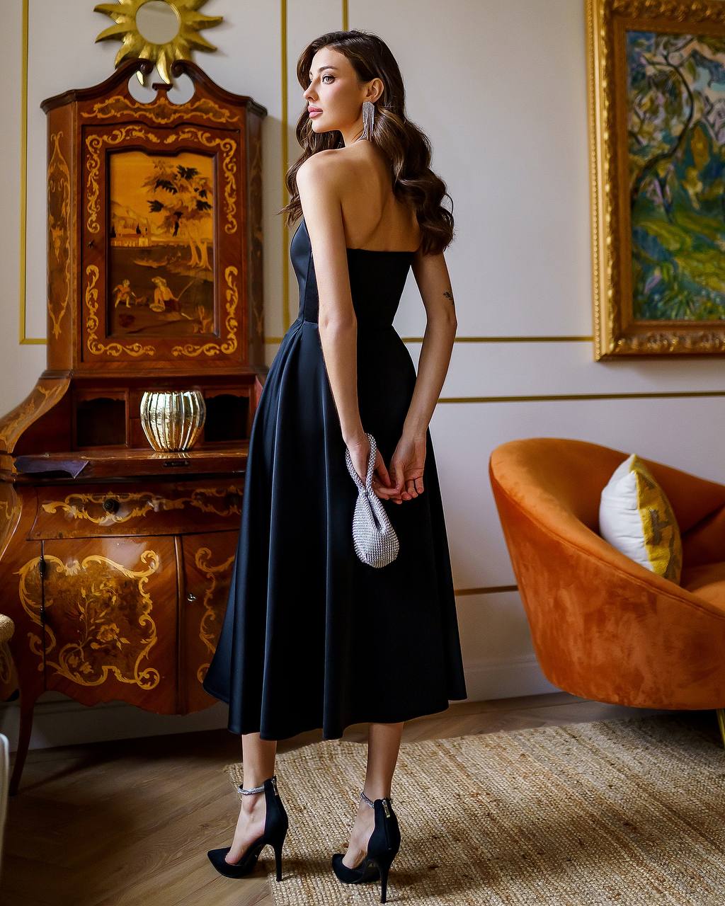Woman in a black dress standing in an elegant room with decorative furniture and art.