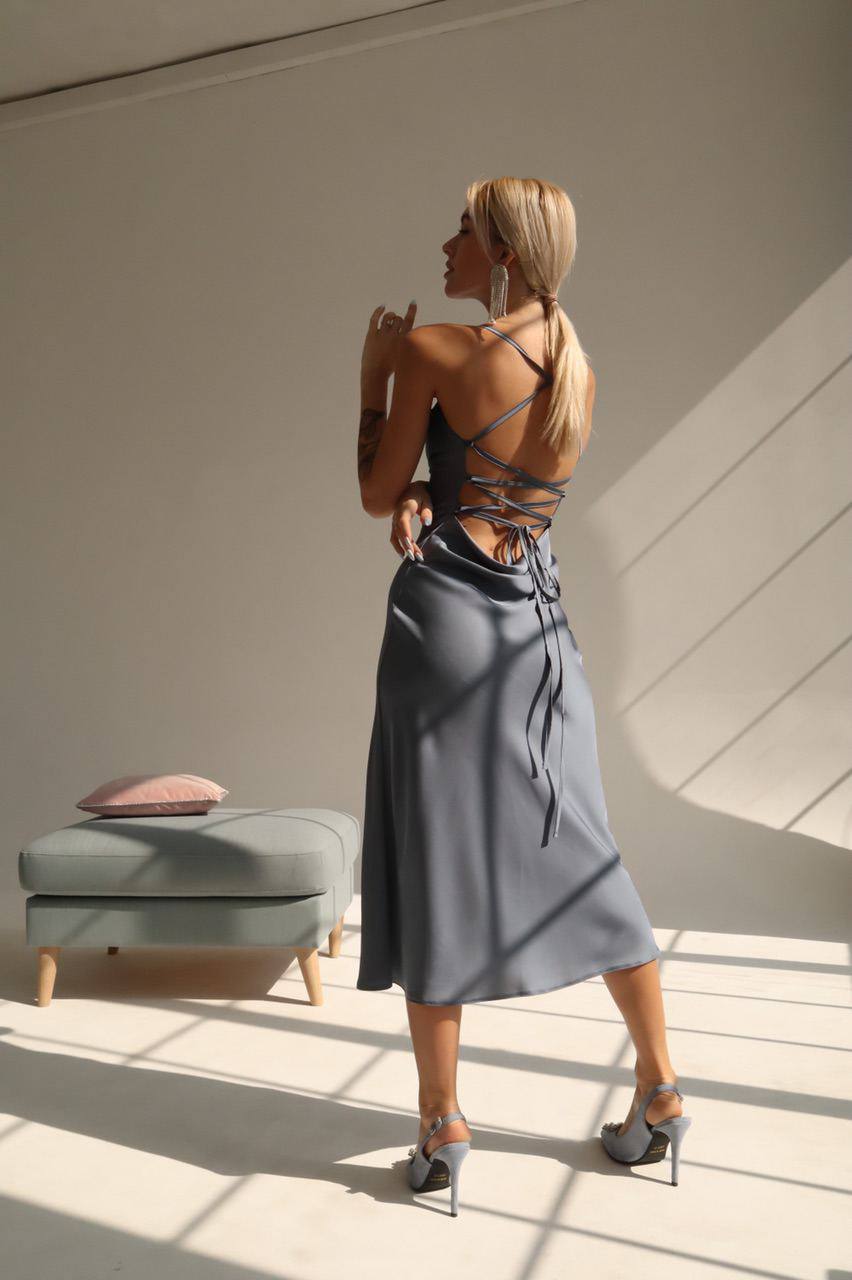 Woman in a gray dress standing in a sunlit room with a minimalistic background