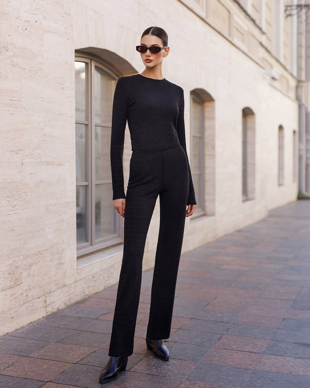 Person wearing a black outfit standing on a sidewalk with a building in the background