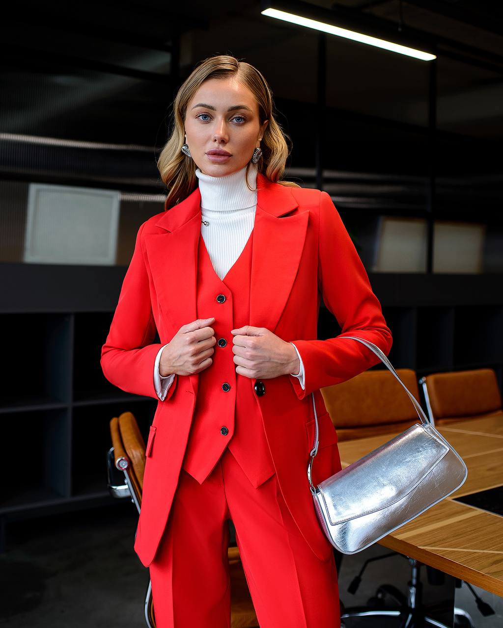 Woman in a red suit with a silver handbag in an office setting